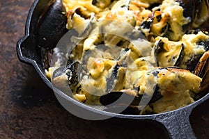 Frying pan with mussels under cheese sauce on a brown background close-up
