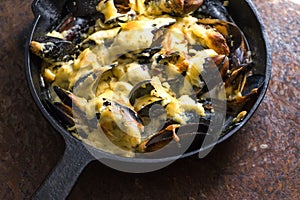 Frying pan with mussels under cheese sauce on a brown background side view