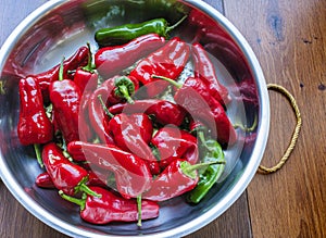 Frying pan with organic red and some green peppers on a wooden board.