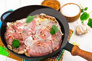 Frying pan with piece of raw meat with spices on white wooden table