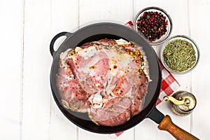 Frying pan with piece of raw meat with spices on white wooden table