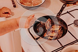 Frying pan with roasted steaks meat on fire at domestic kitchen. Female hands with fork turning meat