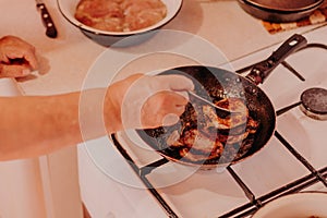 Frying pan with roasted steaks meat on fire at domestic kitchen. Female hands with fork turning meat