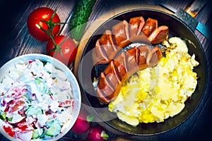 Frying pan with sausages, eggs, a plate with salad, on a wooden tray