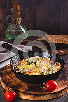 Frying pan with scrambled eggs with broccoli and tomatoes on a wooden board vertical view