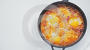 Frying pan with shakshuka with cheese rotates in a circle on a white background