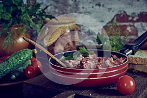 A frying pan with stewed meat seasoned with fresh herbs on a wooden countertop.