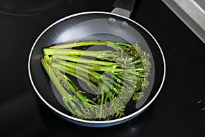 Frying pan with tasty cooked broccolini on cooktop, closeup