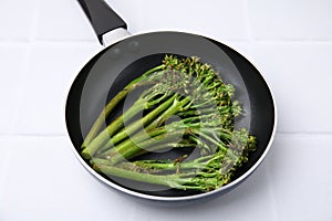 Frying pan with tasty cooked broccolini on white tiled table