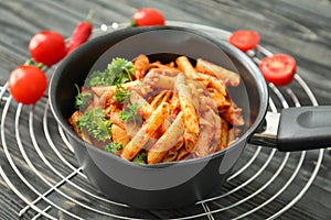 Frying pan with tasty penne pasta and tomato sauce on cooling rack