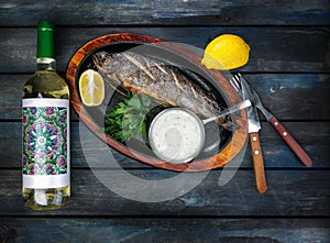 Frying pan with tasty trout fish on wooden background with a bottle of wine greens, sauce and lemon.