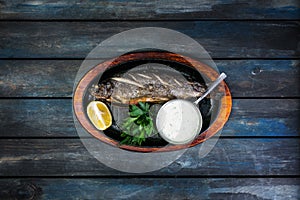 Frying pan with tasty trout fish on wooden background wine greens, sauce and lemon