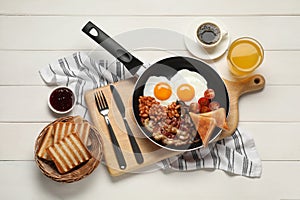 Frying pan with traditional English breakfast on white wooden table, flat lay