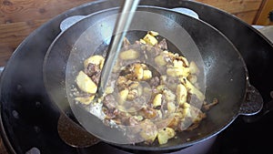 Frying of potatoes with meat, onions and tomatoes in a kazan on a gas grill