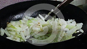 Frying and stirring onion in olive oil. Onion is frying in a black frying pan