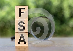 FSA abbrevation on wooden blocks on table with magnifier on green background. Business concept