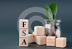 FSA - acronym on wooden cubes on the background of a glass jar with coins and green leaves