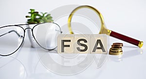 FSA concept on wooden cubes and flower ,glasses ,coins and magnifier on the white background