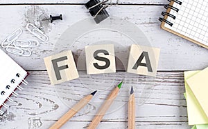 FSA text on wooden block with office tools on the wooden background