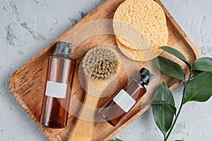 Fsce and body care spa treatment consept. Two brown unbranded bottles, face brush and sponges on wooden tray. Unbranded packaging