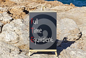 FTE Full time equivalent symbol. Concept words FTE Full time equivalent on beautiful black chalk blackboard. Beautiful stone beach