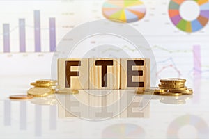 FTE the word on wooden cubes, cubes stand on a reflective surface, in the background is a business diagram