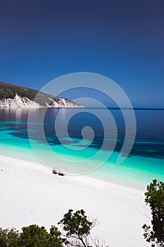 Fteri beach Kefalonia, Greece. Family under umbrella on pebble beach. Clear blue azure emerald sea water in lagoon