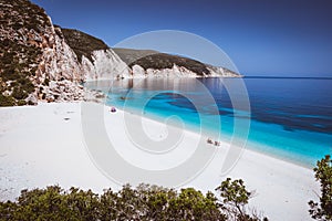 Fteri beach, Kefalonia, Greece. Lonely tourists protected from sun umbrella chill relax near clear blue emerald