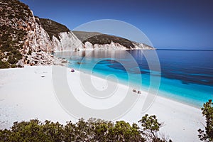 Fteri beach, Kefalonia, Greece. Lonely tourists protected from sun umbrella chill relax near clear blue emerald photo