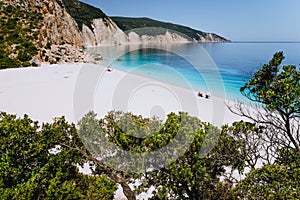 Fteri beach, Kefalonia, Greece. Lonely tourists under umbrella chill relax near clear blue emerald turquoise sea water