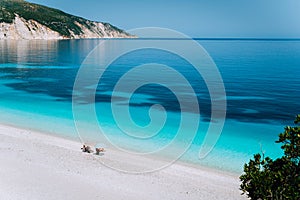 Fteri beach, Kefalonia, Greece. Lonely unrecognizable tourist couple hiding from sun umbrella chill relax near clear photo