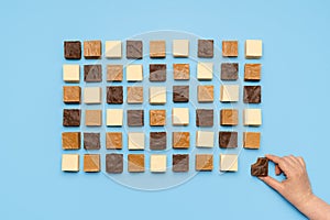 Fudge assortment aligned symmetric on blue table. Woman grabbing chocolate fudge, top view