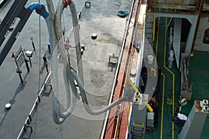 Fuel hose of bunker barge attached to crane and connected to container vessel in bunker station.