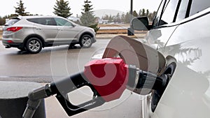 Fuel nozzle with red handle, filling gas tank of white car