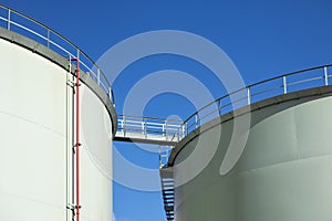 Fuel storage tanks with catwalk bridge against blue sky