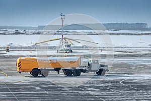 fuel tanker truck rides on the taxiway at the airport against the background of a helicopter at winter time