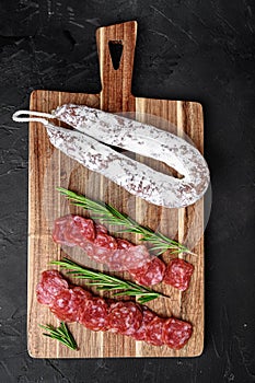 Fuet salami wurst cut in slices and whole sausage on black background, top view