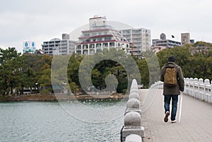 Fukuoka, Japan - January 1, 2019: A man carrying backpack and holding white umbrella walking on the stone bridge in Ohori Park