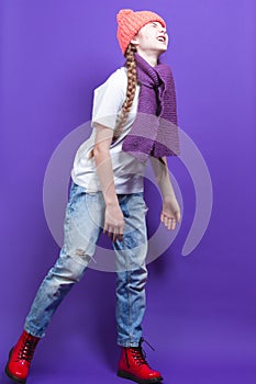 Ful Length Portrait of Caucasian Teenager Girl in Coral Warm Knitted Winter Hat and Violet Scarf Moaning Over Purple Background