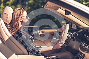 A fulfilled young woman driving a convertible during sunset. Wind in hairs photo