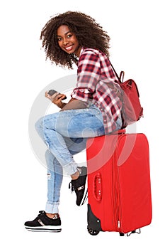 Full body beautiful african woman with phone sitting on suitcase and smiling over white background