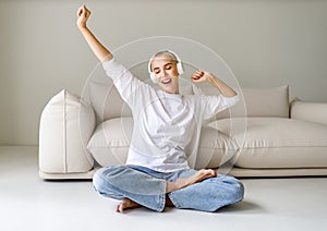 Beautiful woman meloman with very short hair listens to music and sings near couch photo