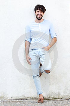 Full body handsome young man leaning against white wall and smiling