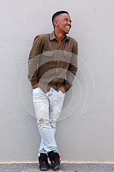 Full body happy black man leaning against gray wall