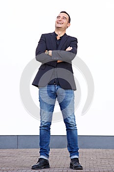 Full body happy man in 30s laughing against white wall with arms crossed