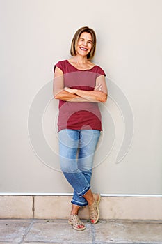 Full body happy older woman leaning against wall