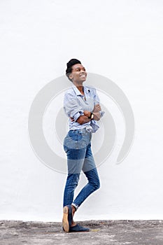 Full body happy young black woman leaning against wall looking up