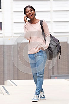 Full body happy young black woman walking and talking with mobile phone