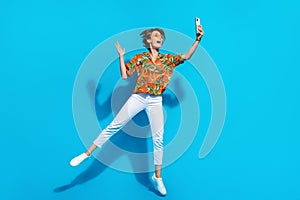 Full body photo of active excited lady jumping hold smart phone take selfie arm waving isolated on blue color background