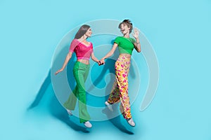 Full body photo advert promo two girls waving arm greetings positive mood hands together jump trampoline isolated on